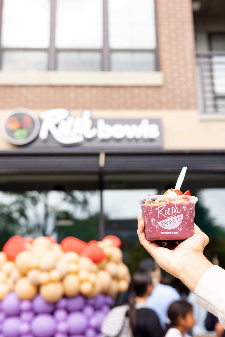 Someone holding a rush bowls bowl infront of a franchise location - join Rush Bowls.